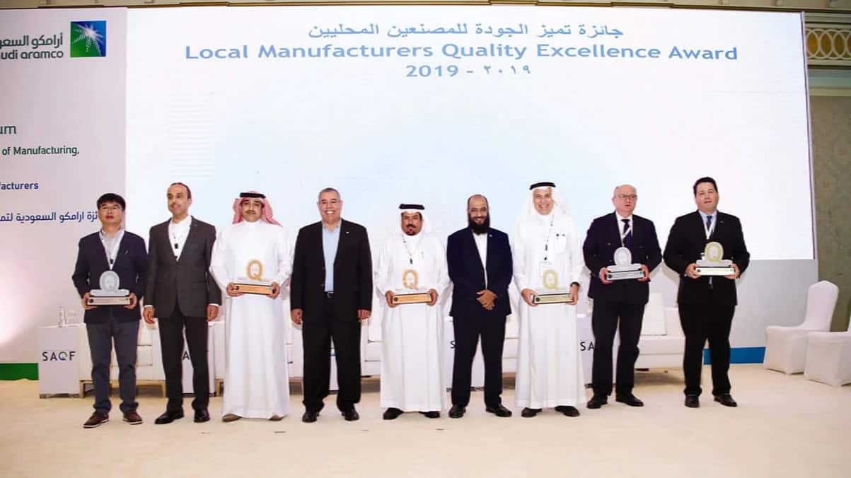 Group of men in formal attire holding awards at a quality excellence event in Saudi Arabia.